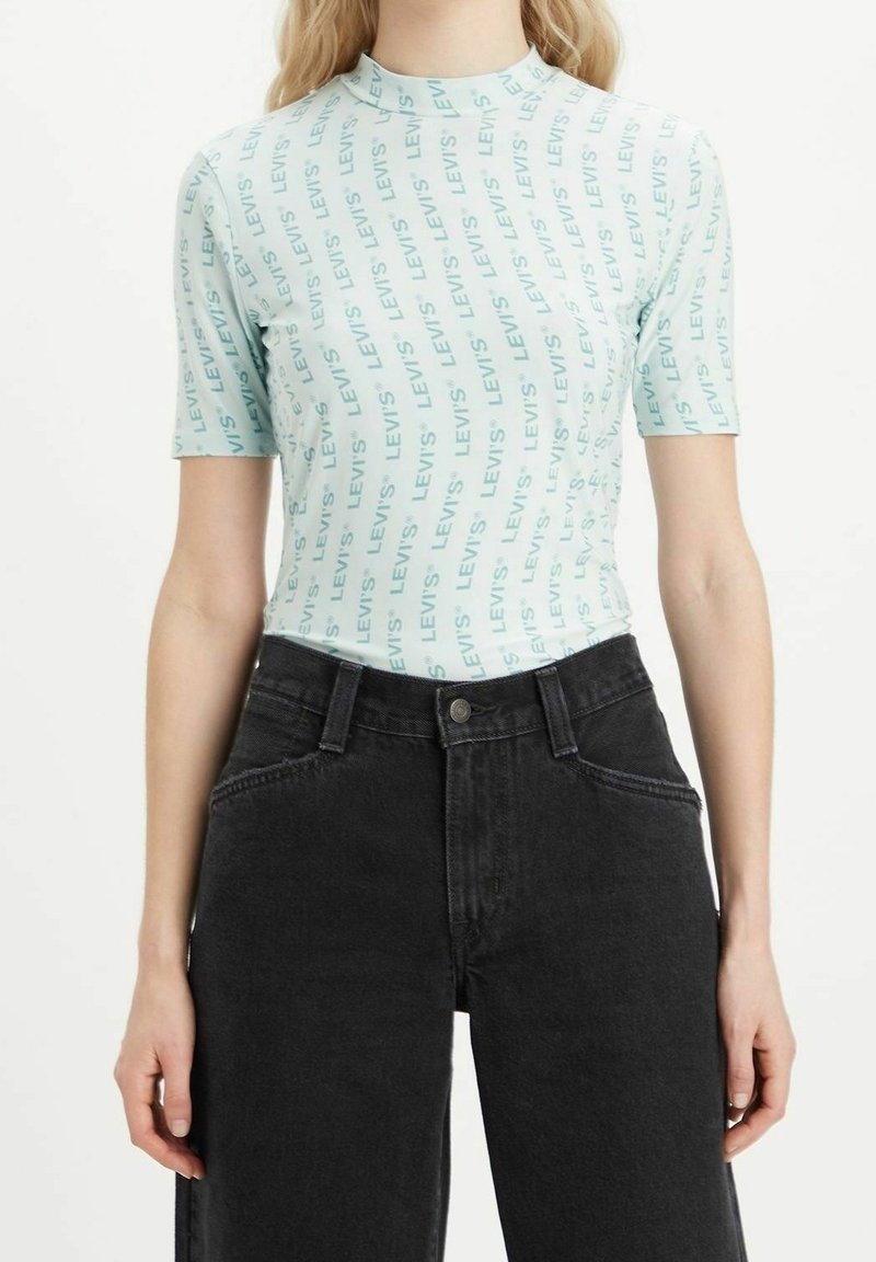 Světle modré obepnuté tričko s opakujícím se vzorem textu "LEVI'S"; spárované s černými džíny s vysokým pasem. Krátký rukáv, hladká textura.