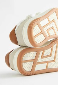 Baskets avec une tige en daim beige, un talon en cuir marron et une semelle en caoutchouc texturée avec un motif géométrique.