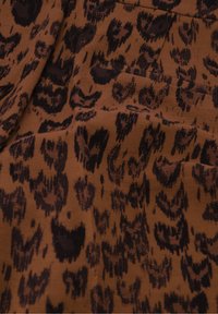 Bruine stof met een zwart panterprintpatroon met variërende vormen en texturen, met een zachte, gestructureerde oppervlakte.