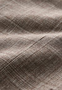 Gros plan sur un tissu marron texturé avec un motif de quadrillage subtil et des coutures visibles.