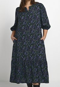 Lång svart klänning med ett blommönster i blått och grönt. Har en mandarin-krage, sänkta axlar och sidofickor.