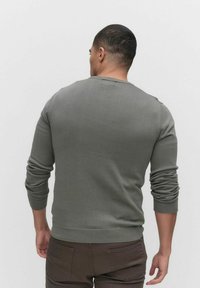 Grå stickad tröja med långa ärmar, ribbade muddar och nederkant, rund halsringning. Bakvy visar en figurnära design och mjuk yta.