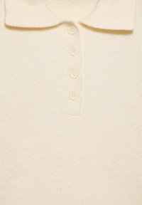 Polo shirt tricotat de culoare crem, cu un guler larg și patru butoane asortate pe fața plăcuței.