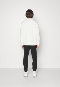 Valkoinen collegepaita, mustat juoksuhousut ja valkoiset lenkkarit. Collegepaidassa on pyöreä kaulus ja juoksuhousuissa on kapeampi leikkaus.