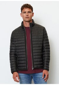 Chaqueta de plumas negra con un alto cuello, diseño acolchado, zipper frontal y bolsillos laterales, llevada sobre una camisa burdeos, exhibida sobre un fondo blanco.