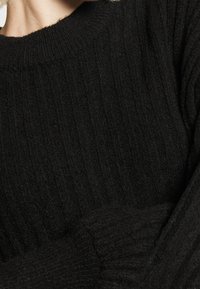 Svart ribbad tröja med hög krage. Mjuk textur med synligt stickat mönster och långa ärmar med ribbade muddar.