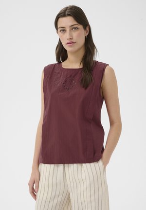 Femme portant un haut sans manches violet foncé avec broderie florale, associé à un pantalon crème taille haute avec fines rayures verticales.