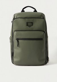 Olíva zöld hátizsák sima, tartós anyagból; elején cipzáras zsebbel, felső fogantyúval és fekete cipzár díszítéssel.