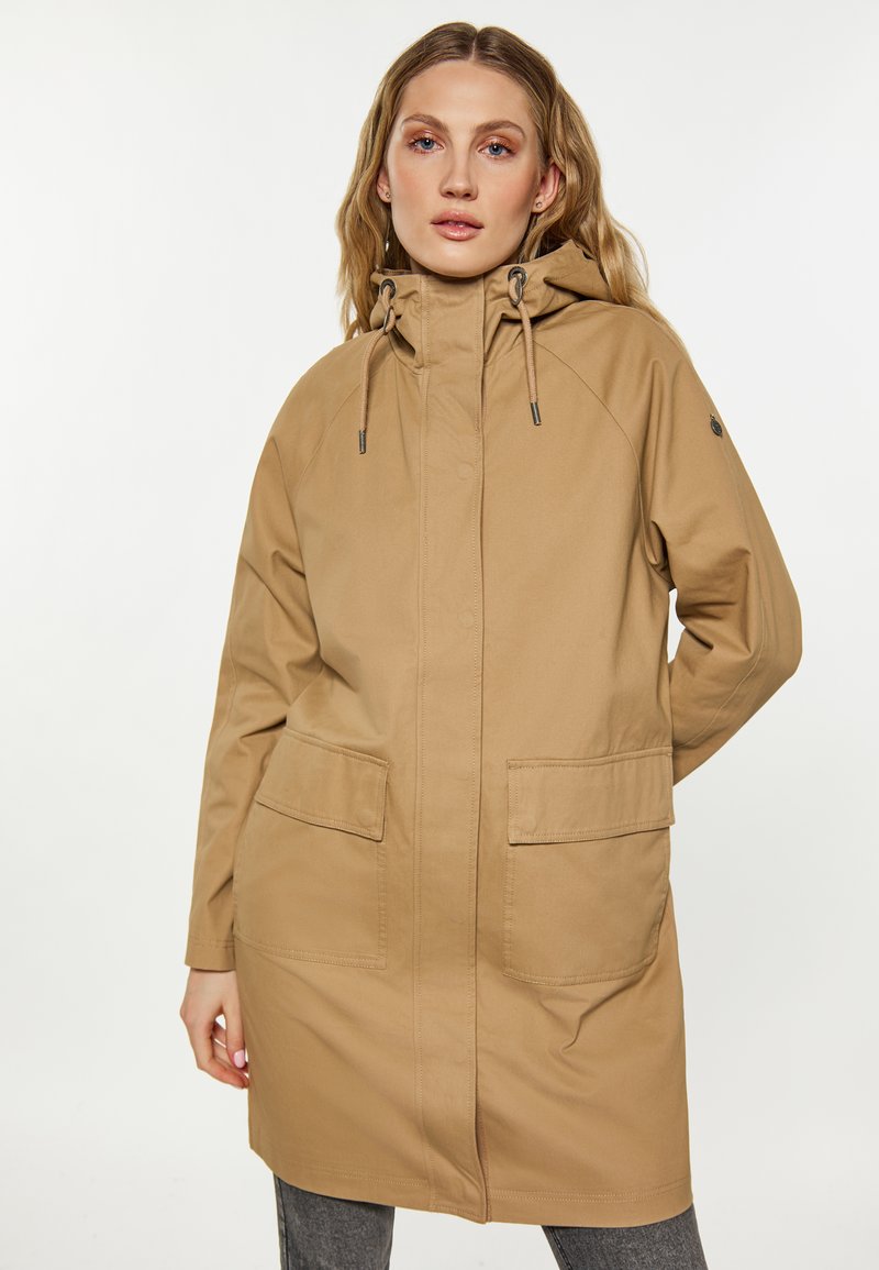 Veste d'extérieur beige avec capuche, présentant une coupe droite, deux poches avant, des ajustements par cordon et une texture lisse et mate.