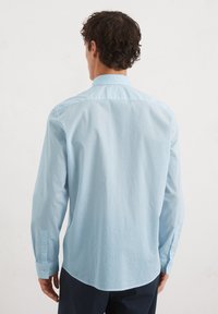 Lichtblauw overhemd met lange mouwen, voorzien van een gestructureerd patroon, een button-down kraag en verstelbare manchetten. Getailleerde pasvorm met een gebogen onderrand.