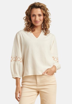 Crème-kleurige blouse met een V-hals en ballonmouwen, voorzien van geborduurde details in een roestkleur op de manchetten. Zachte, gemêleerde stof.
