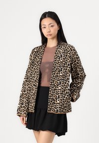 Leopard print jacket made of soft fabric, featuring a loose fit and open front design, paired with a brown top and black skirt.