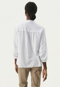 Witte linnen blouse met driekwart mouwen, geplooide achterkant en subtiele verticale strepen op de mouwen. Heeft een ronde halslijn en een relaxte pasvorm.