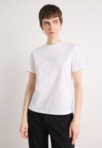 White cotton t-shirt with a round neckline and short sleeves. Features a light blue "Calvin Klein" logo embroidered on the chest.