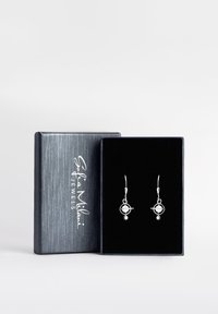 Silvriga örhängen med cirkulärt och stjärnmönster, uppställda i en ask klädd i svart sammet med en strukturerad grå utsida.