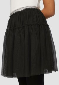 Zwarte gelaagde tule rok met een geraffineerde tailleband met glinsterende rand. Transparante textuur, kniehoogte, met een volumineuze silhouet.