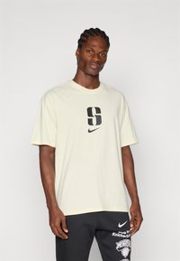 Kreemikas t-särk, lühikeste varrukatega, ümar kaelus, esiosas suur must "S" graafika ja Nike logo trükitud.