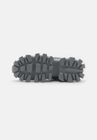 Gray athletic shoe outsole featuring a rugged tread pattern with thick lugs for grip and angular shapes for traction on various surfaces.