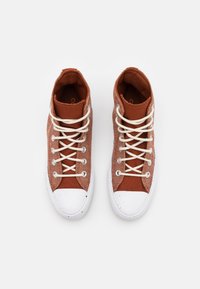 Zapatillas altas de lona en color óxido, con puntera de goma blanca y cordones crema, y detalles texturizados en los laterales.