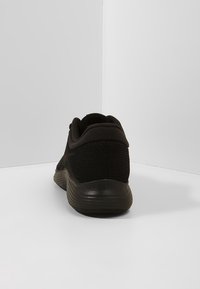 Musta urheilujalkine, jossa on verkkopäällinen, pehmustettu kantapää ja kumipohja. Sujuva koostumus, jossa on minimaalista korostusta ja virtaviivainen muotoilu.