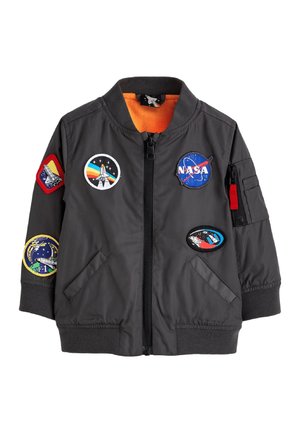 Veste bomber grise avec doublure orange, fermeture éclair et plusieurs patchs à thème NASA. Comprend des poignets et un ourlet côtelés, ainsi que des poches latérales.