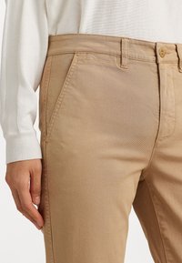 Béžové nohavice z bavlnenej zmesi so slim fit strihom, s bočnými vreckami, pásom na gombík a hladkou textúrou.