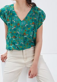 Grüne Bluse mit floralem Muster, V-Ausschnitt, kurzen Ärmeln und Raffungselementen. Leichtes Material mit verschiedenen Blumen- und Blattmotiven.