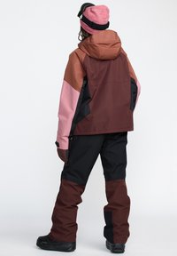 Vêtements d'extérieur résistants à l'eau avec un design bicolore en marron, rose et noir. Comprend une capuche et des gants texturés.