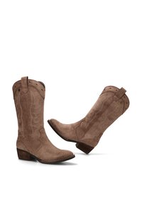 Par de botas de vaquero marrones de ante hasta la pantorrilla con patrones de llamas bordados y tacones de madera apilados bajos sobre un fondo blanco.