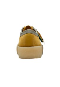 Gul mockasinsneaker med en grå textilkrage och en tjock beige sula. Har rundad form och dekorativa pärlor på sidan.