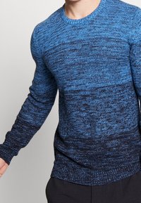 Maglione blu lavorato a maglia con un gradiente dal blu chiaro al blu scuro, maniche lunghe, collo rotondo e tessuto testurizzato.