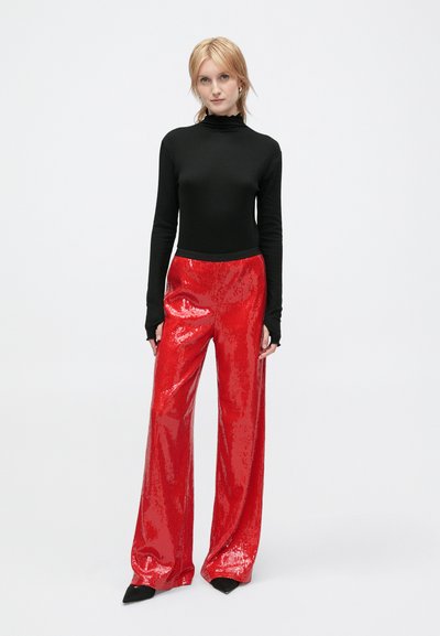 Haut noir ajusté à manches longues associé à un pantalon large en sequins rouges brillants. La tenue présente une texture lisse et une silhouette simple.