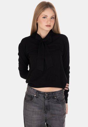 Maglione corto nero con dettaglio del fiocco legato, realizzato in un tessuto morbido. Presenta maniche lunghe e un collo rotondo, abbinato a jeans di denim scuro.