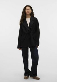 Mustmustri mustriga, kahe esipocketiga ja nurgelise kaelusega. Kantud kerge topi peal ja kombineeritud laia jalgadega tumedate teksadega.