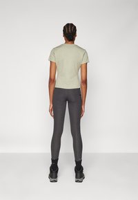 Green short-sleeve t-shirt paired with dark gray leggings; fitted design, smooth texture, contrasting stitching, and black footwear.
