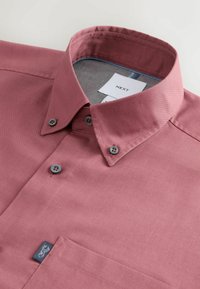 Koszula z kołnierzykiem na guziki w ciemnym różowym kolorze, z przednią kieszenią i oznaczeniem marki, pokazująca górne guziki oraz wewnętrzną metkę z napisem NEXT.