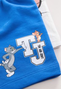 Blå bomullst-shirt med tecknade karaktärer Tom och Jerry. Inkluderar vit grafisk text "TJ" med "TOM AND JERRY" under, mjuk textur.