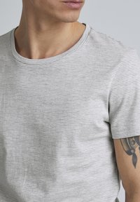 Harmaa raidallinen lyhythihainen t-paita, joka on valmistettu pehmeästä kankaasta. Pyöreä pääntie ja slim fit -muotoilu ovat näkyvissä, korostaen kankaan rakennetta ja kuvioita.