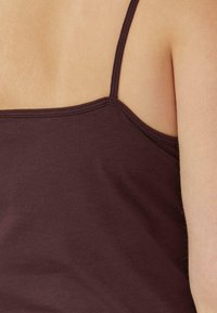 Bordeauxrood tanktop met dunne bandjes, gemaakt van zacht katoenen stof. Heeft een aansluitende pasvorm en een gladde textuur, zonder zichtbare patronen.