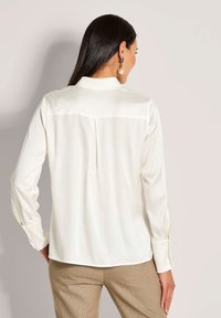 Witte blouse met lange mouwen, een rugplooi, zachte textuur en een afgeronde zoom, gecombineerd met textuurbare beige broek.