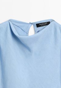 Blusa azzurro chiaro che mostra la scollatura posteriore con una piccola chiusura con bottone e un'etichetta Massimo Dutti all'interno.