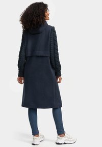 Lange navy hoodie met kabelgebreide mouwen. Gemaakt van zacht materiaal, heeft een relaxte pasvorm en capuchon. Gecombineerd met skinny jeans en sneakers.