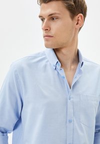 Lyseblå skjorte med knaplukning, lavet af et blødt stof, med krave, lille brystlomme og matchende knapper. Glat tekstur, lange ærmer.