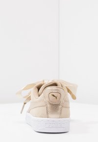 Baskets en cuir suédé beige clair avec une semelle en caoutchouc blanche, des lacets en satin et un logo doré sur le talon. Texture lisse et design bas.