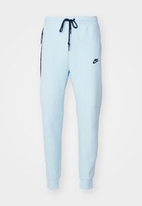 Light blue Nike sweatpants with black logo, featuring an elastic waistband, side pockets, and tapered cuffs. Soft fabric and smooth texture.