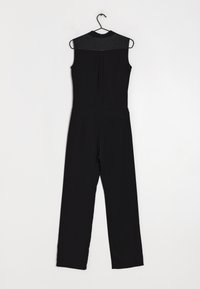 Tuta nera con design senza maniche, texture liscia. Presenta un colletto in satin, spacco posteriore e tasca laterale. Appesa a un gancio nero.
