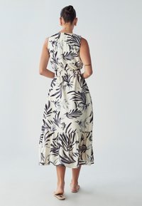 Maksi obleka brez rokavov, ki ima svetlo bež ozadje s črnimi cvetličnimi vzorci. Elastičen pas, nabran rob in tekoč material.