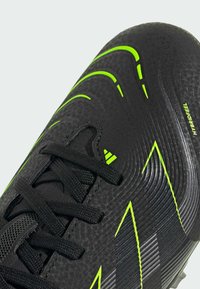 Czarne buty piłkarskie z teksturowaną powierzchnią, zielonymi i szarymi akcentami, czarnymi sznurowadłami oraz opływowym kształtem. Posiadają branding "HYBRIDFEEL".