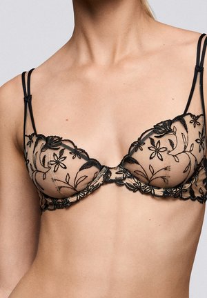 Doorzichtige zwarte kanten beha met bloemrijke borduursels en dubbele dunne schouderbandjes, gedragen op een torso met een lichte huidtint.
