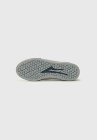 Semelle de sneaker blanche avec un motif en alvéoles et un logo bleu. Matériau en caoutchouc texturé, bout arrondi, profil plat et détails minimaux.